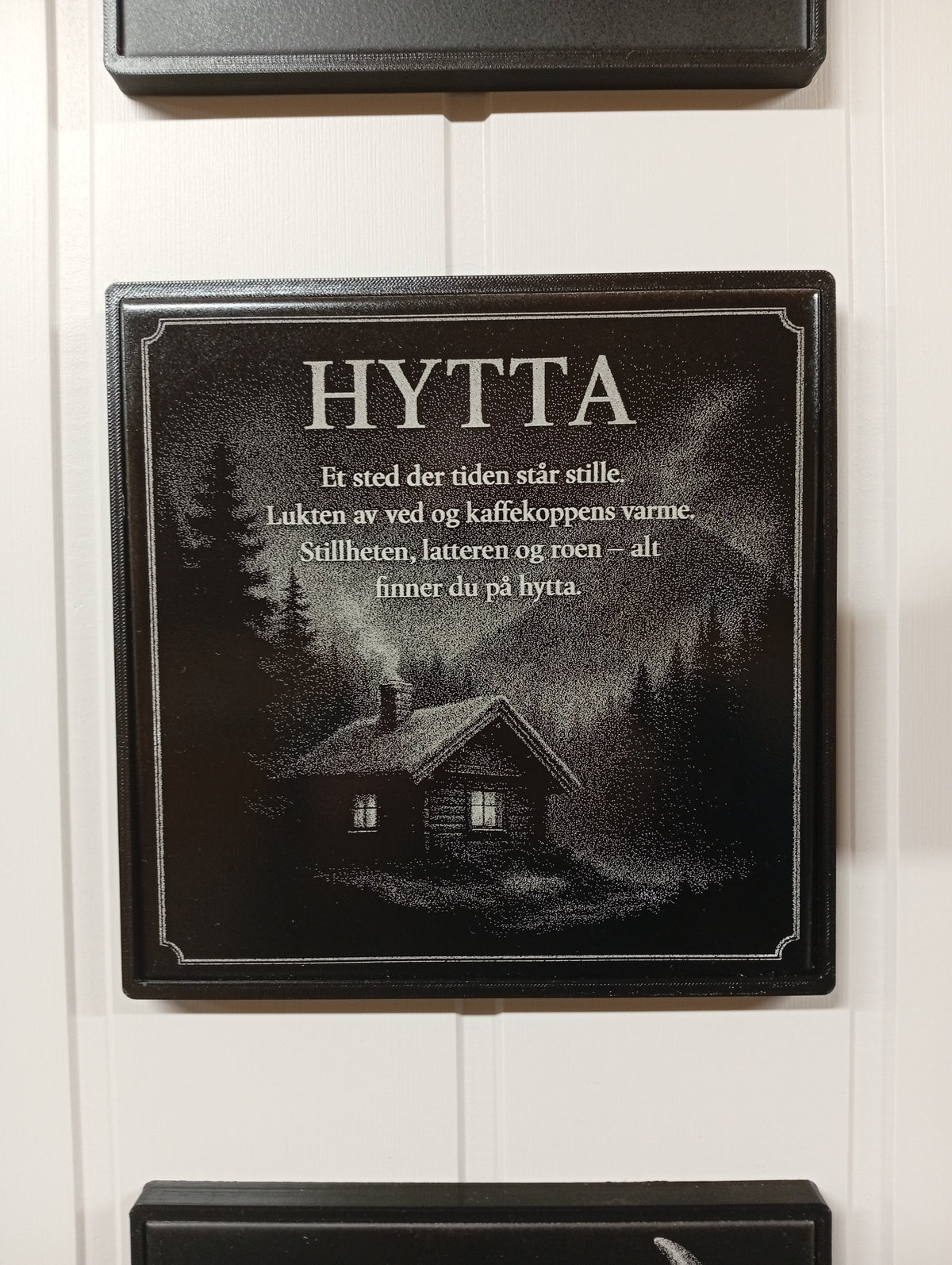 Lasergravert dekorplate til hytta i svart keramisk flis med teksten «HYTTA – et sted der tiden står stille